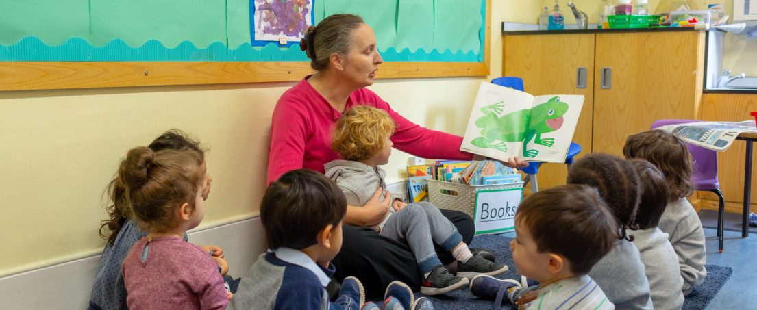 teacher reading a book with a frog over the pages