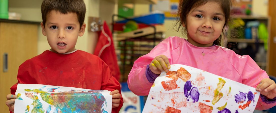 2 kids holding up painted pieces of paper